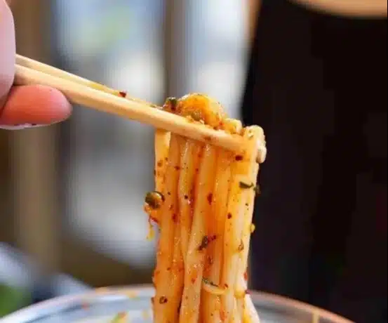 Plate of spicy potato noodles garnished with herbs and chili peppers