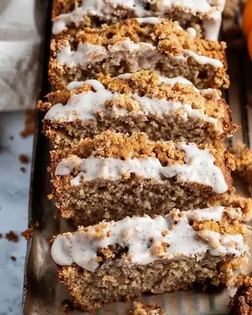 Slice of pumpkin bread topped with cream cheese frosting on a wooden table