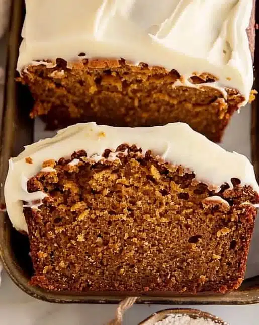 Sliced pumpkin bread topped with cream cheese frosting on a plate