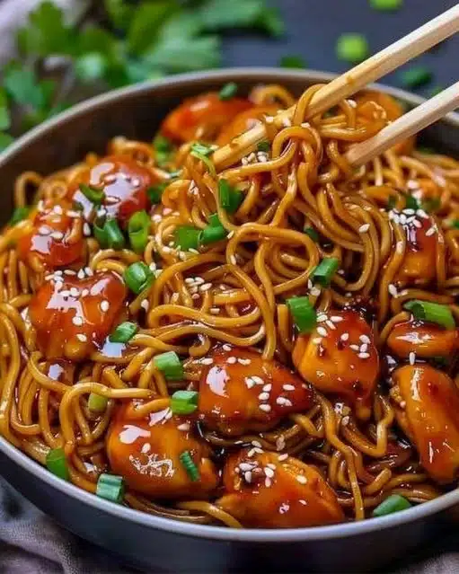 Plate of sticky garlic chicken noodles topped with green onions and sesame seeds
