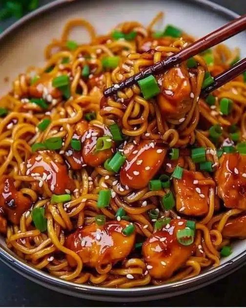 Delicious Sticky Garlic Chicken Noodles in a bowl with fresh herbs and spices.