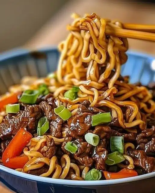 A bowl of sticky Hoisin beef noodles garnished with green onions and sesame seeds.