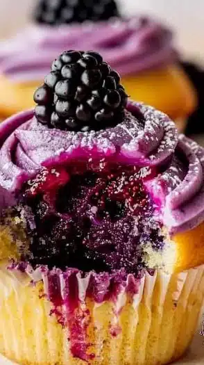 Lemon berry cupcakes with blackberry filling and purple frosting on a decorative plate.