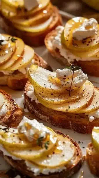 Delicious pear, goat cheese, and honey crostini appetizer on a wooden board.