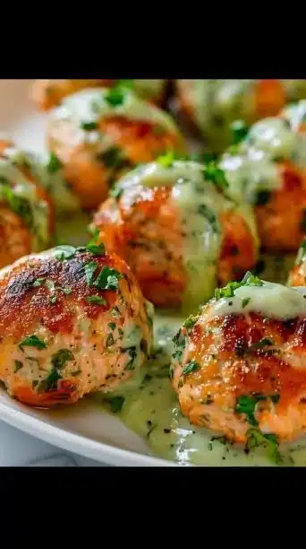 Baked salmon meatballs drizzled with creamy lemon-dill sauce on a plate