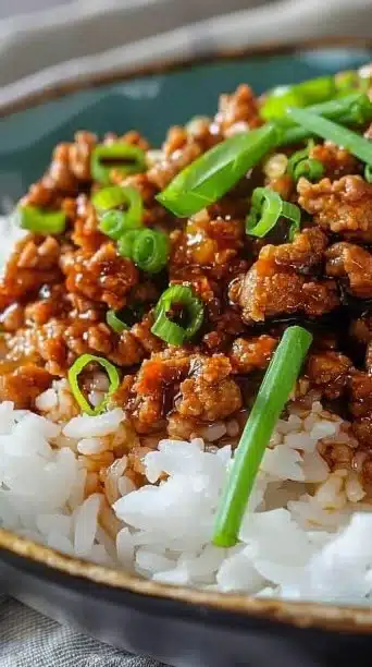 Plate of ground orange chicken garnished with green onions and served with rice.