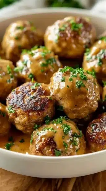 Slow-cooked Swedish meatballs served with creamy sauce and parsley garnish.
